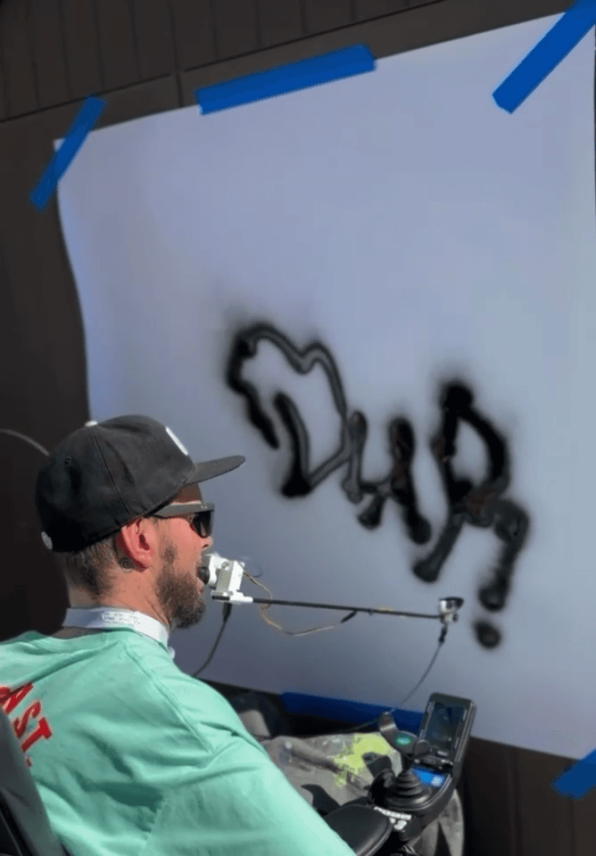 Benny Diar using a assistive mouth controlled spray painting device while in a wheelchair.